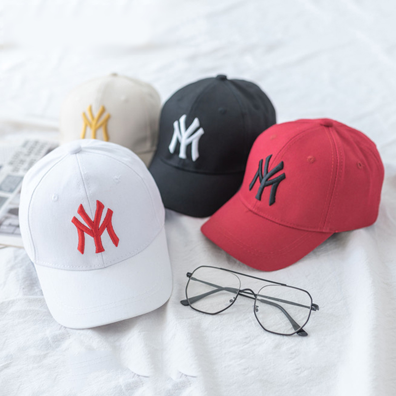 quatre casquettes de baseball blanche rouge noire et beige avec une écriture brodée MY sur u, drap blanc avec des lunettes de vue