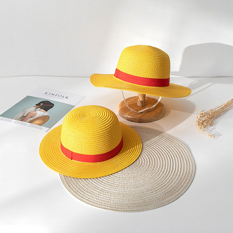 Deux chapeaux en paille ronds avec liseré rouge, les deux sont jaunes, et ils sont posés sur un sol blanc sur un rond gris
