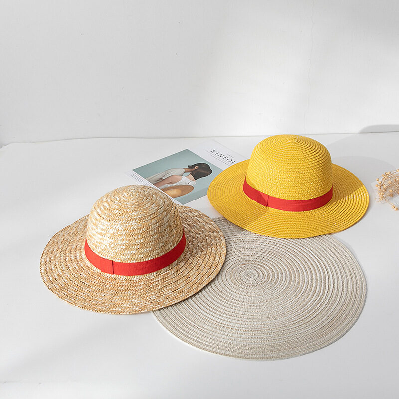 Deux chapeaux en paille ronds avec liseré rouge, l'un est jaune et l'autre blanc, et ils sont posés sur un sol blanc sur un rond gris