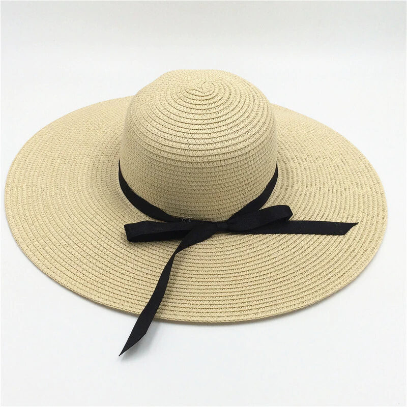 chapeau beige avec un ruban noir, à grand bord, en paille pour l'été pour femmes et présenté sur fond blanc
