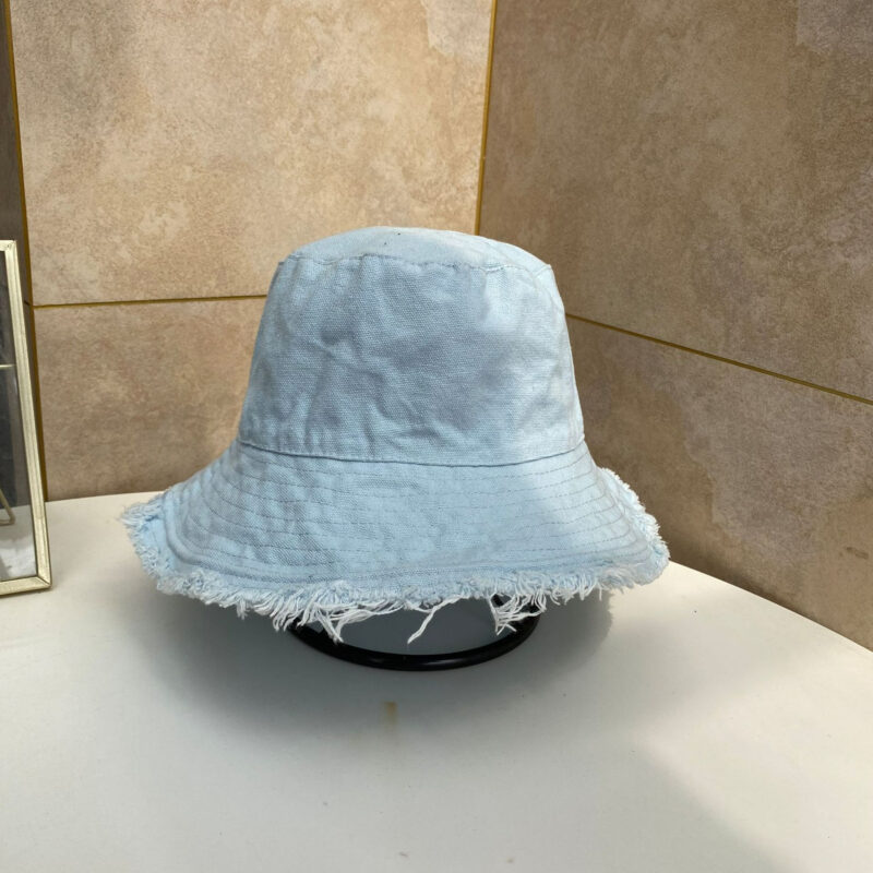 Chapeau bob bleu clair pastel posé sur un porte-chapeau noir, sur une table blanc cassé, on voit un angle de mur beige derrière le chapeau bob