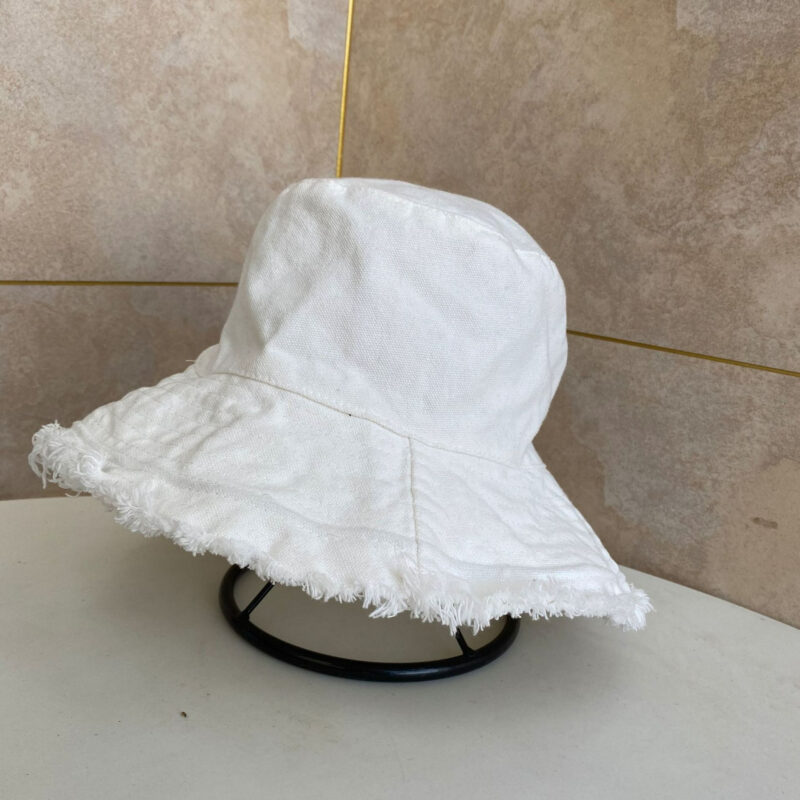 Chapeau bob blanc clair pastel posé sur un porte-chapeau noir, sur une table blanc cassé, on voit un angle de mur beige derrière le chapeau bob