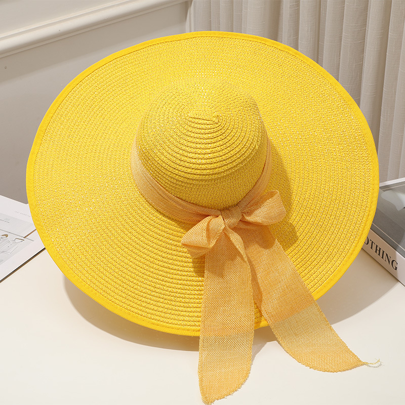 Chapeau de paille jaune pétillant avec ruban et nœud et à large bord décoratif posé incliné sur une table blanche