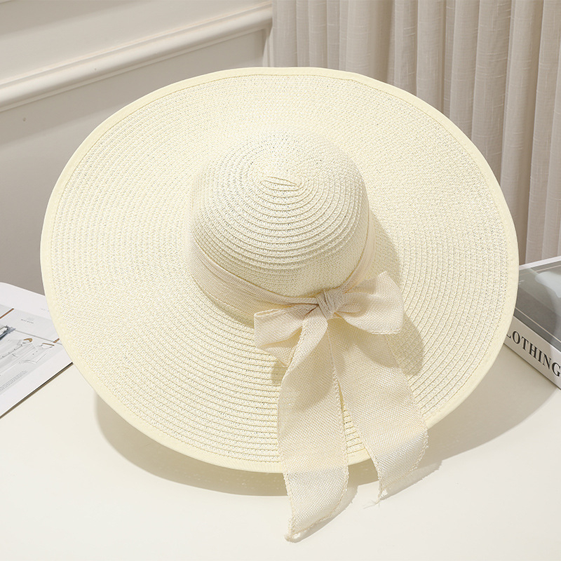 Chapeau de paille blanc pour femme avec ruban et nœud posé sur un porte-chapeau sur une table blanche, vu de haut