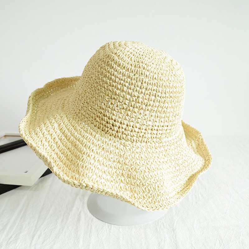 Chapeau de paille à large bord beige posé sur un petit porte-chapeau sur une table blanche