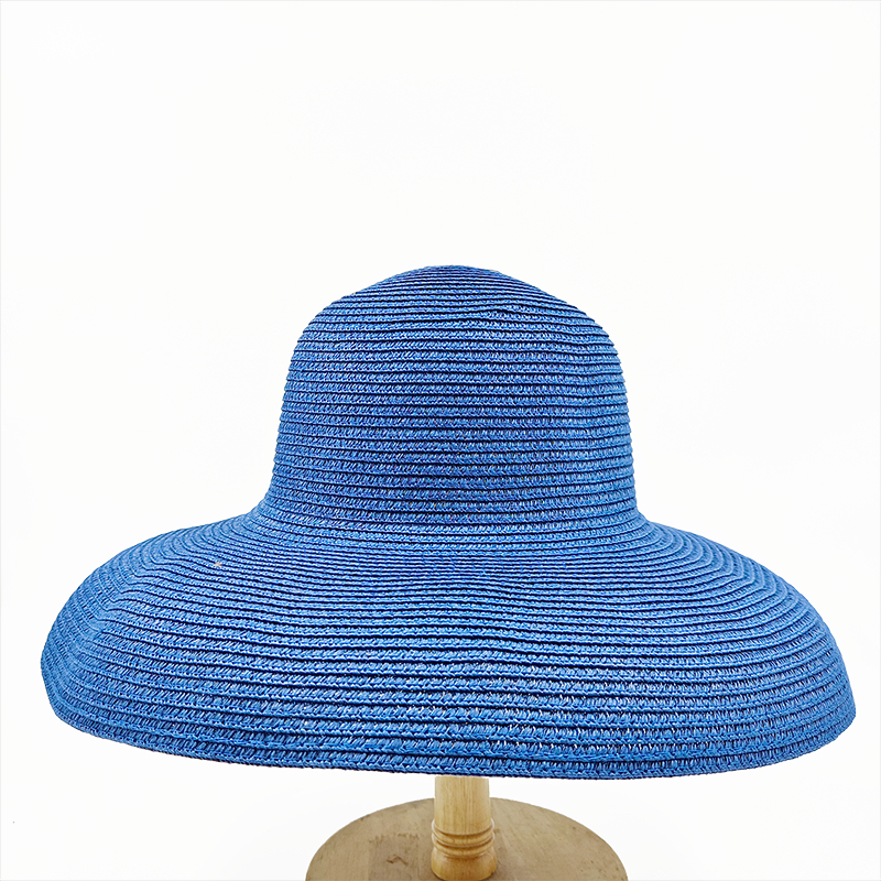 Chapeau bob bleu en paille à large bord retombant posé sur un porte-chapeau en bois avec un socle rond, le tout sur fond blanc