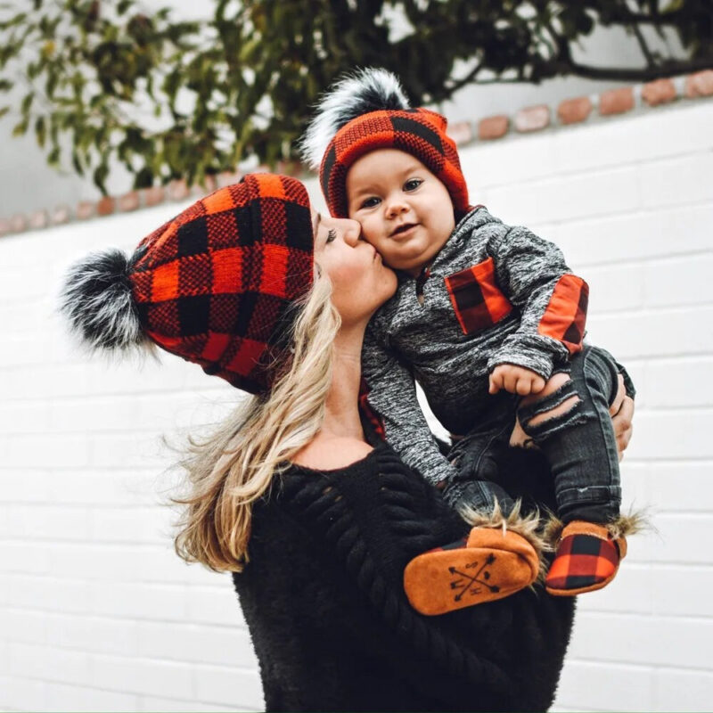 Bonnet Bébé Rouge à Carreaux en Coton sur un bébé dans les bras d'une femme sur fond blanc
