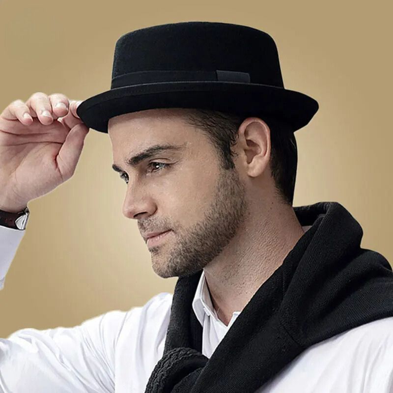 Chapeau Juif Noir Vintage pour Homme, porté par un homme de profil, une main tien le chapeau, il porte une chemise blanche et un pull noir sur les épaules.