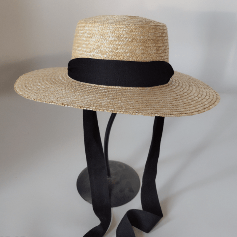 chapeau de paille élégant et rétro avec ruban noir posé sur un support à chapeau, sur fond gris avec des ombres