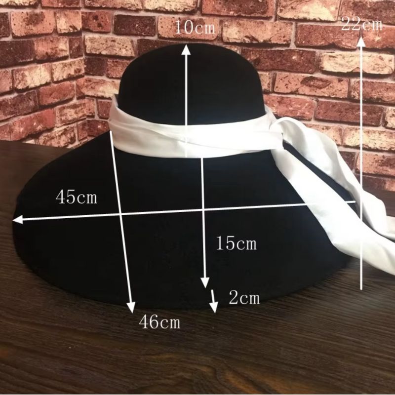 Chapeau pour mariage et cérémonie vintage à large bord noir avec ruban blanc posé devant mur en briques avec les dimensions